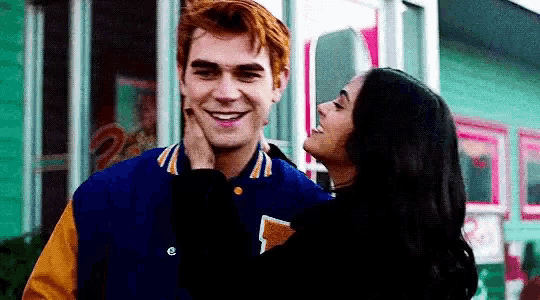 a woman is putting her hand on a man 's face while they are standing next to each other and smiling .