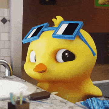 a yellow rubber duck wearing blue square sunglasses sits on a bathroom counter