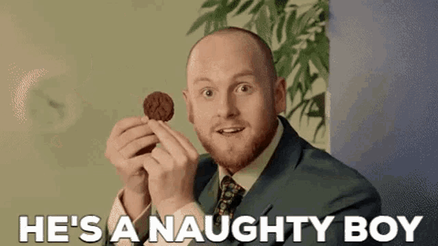 a man in a suit and tie is holding a cookie in his hands and says `` he 's a naughty boy '' .