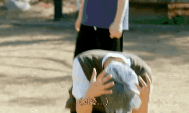 a man is kneeling down with his hands on his head while another man stands in the background .