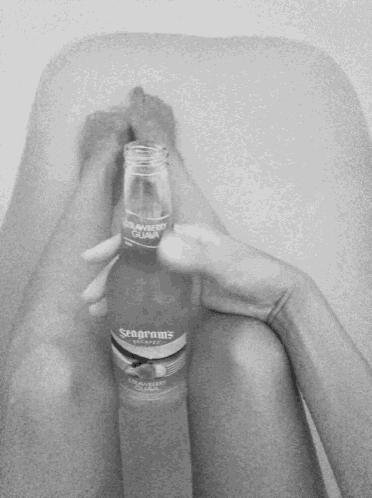 a person in a bathtub holding a bottle of seagrams