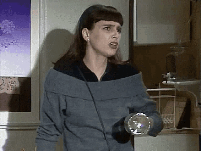 a woman in a sweater is holding a flashlight and making a funny face .
