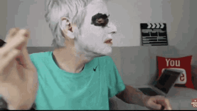 a person with white paint on their face is sitting in front of a laptop