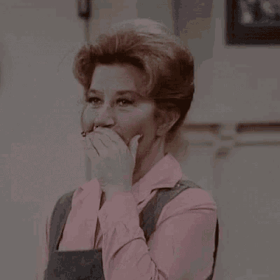 a woman in a pink shirt and grey overalls is smiling .