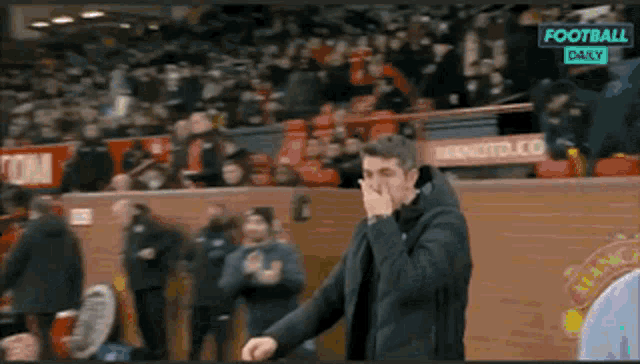 a man covering his nose while watching a football game on a television