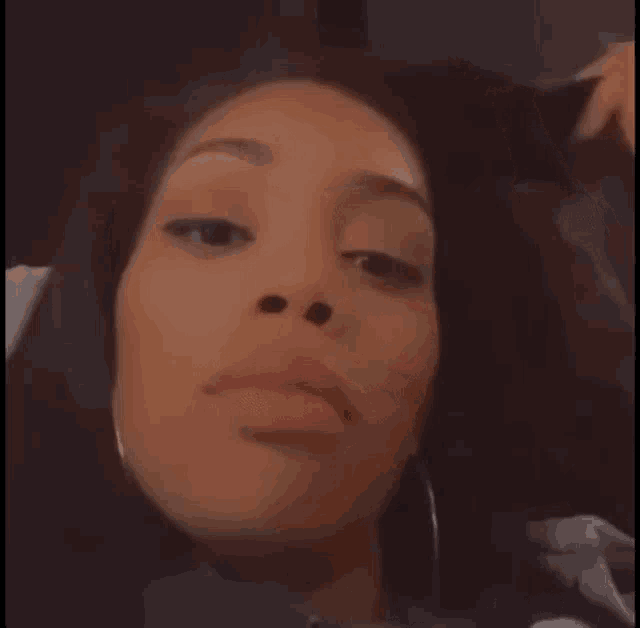 a woman with long black hair and hoop earrings is making a face .