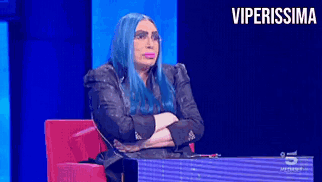 a woman with blue hair is sitting in a red chair with her arms crossed and the words viperissima behind her