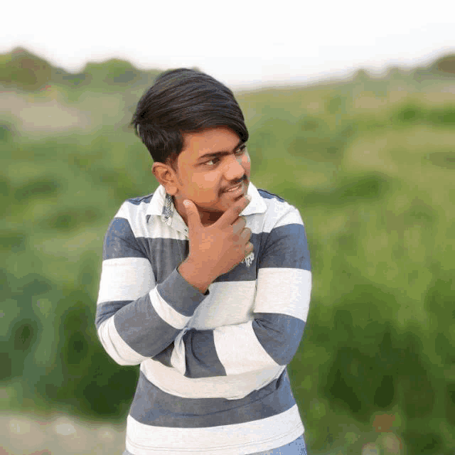 a young man in a striped shirt has his hand on his chin and looks to the side