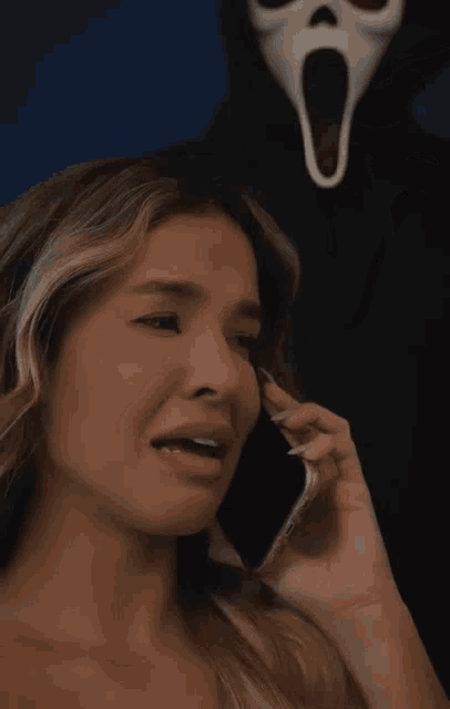 a woman crying while talking on a cell phone in front of a scream mask