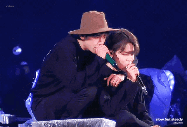 a man in a hat is hugging another man while holding a microphone