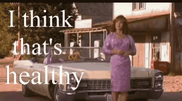 a woman in a purple dress is standing in front of a white car and says i think that 's healthy