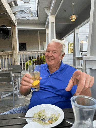 a man in a blue shirt is sitting at a table with a plate of food and a drink in his hand