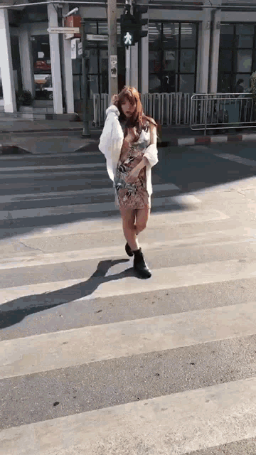 a woman in a dress is crossing a street with a green light