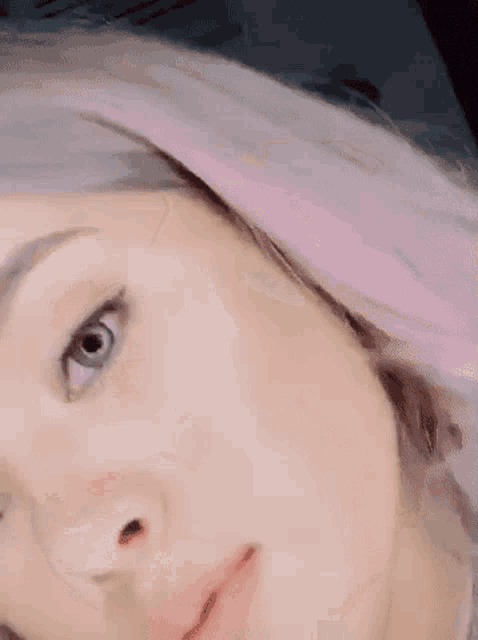 a close up of a woman 's face with pink hair looking at the camera .