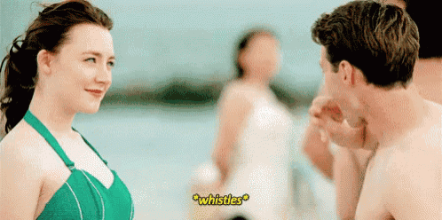 a woman in a green bikini is talking to a shirtless man in front of a group of people .