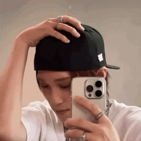 a man wearing a baseball cap is taking a picture of himself in the mirror .