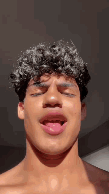 a young man with curly hair is making a funny face with his tongue out