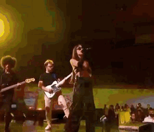 a woman is singing into a microphone on a stage with a man playing a guitar .
