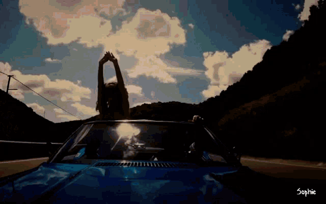 a woman is sitting in a blue car with her arms outstretched and the name sophie on the bottom right