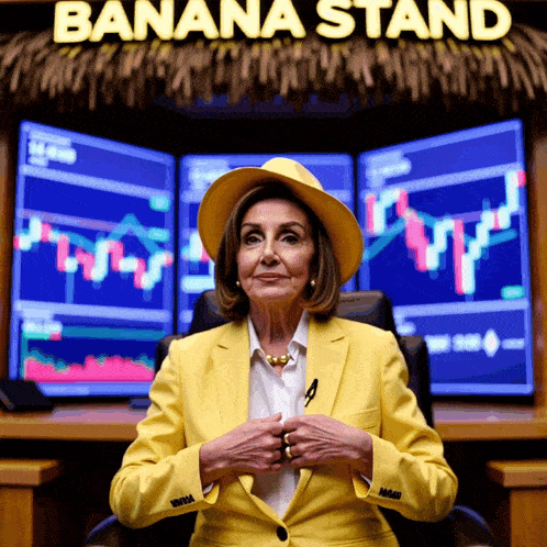 a woman in a yellow suit sits in front of three monitors under a sign that says banana stand
