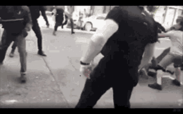 a group of people are standing on a sidewalk fighting each other .