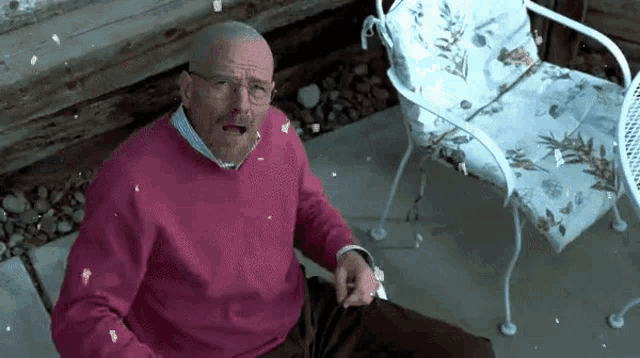 a man in a pink sweater and glasses is sitting in a chair with a chair in the background .