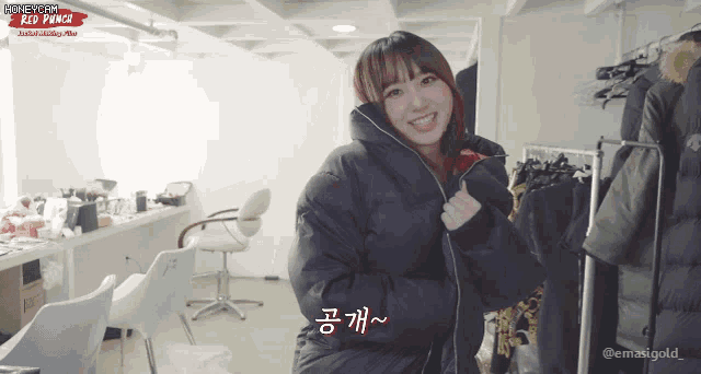 a woman in a black jacket is smiling in a room with a sign that says honeycam red punch