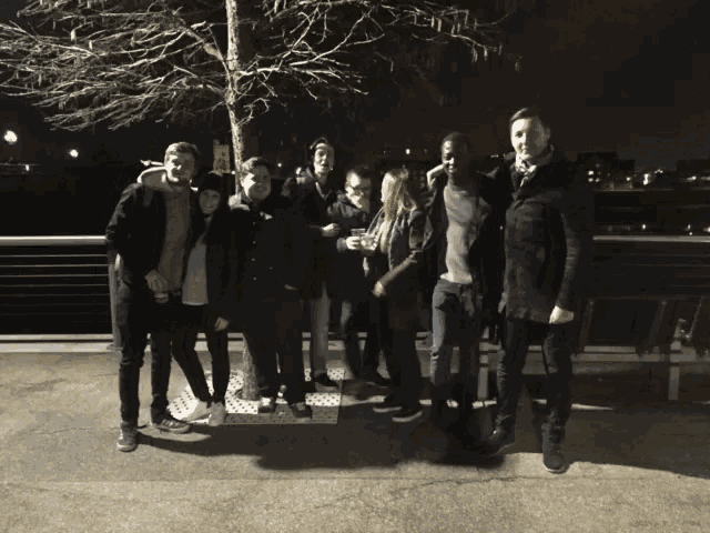 a group of people posing for a picture at night with a tree in the background