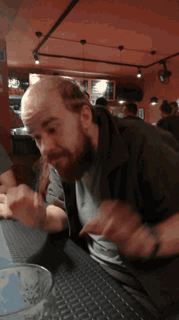 a man with a beard is sitting at a table with a glass of beer in front of him