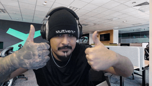 a man wearing headphones and a beanie with the word multivers on it gives a thumbs up