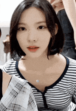 a woman wearing a striped shirt and a blue necklace looks at the camera