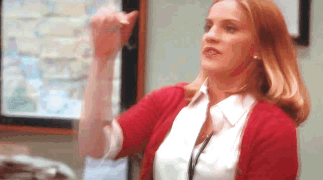 a woman wearing a red sweater and a white shirt is giving a thumbs up
