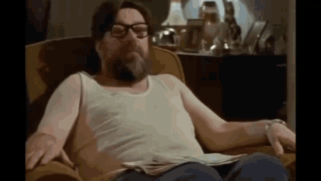 a man with a beard and glasses is sitting in a chair with a newspaper .