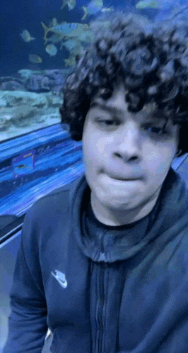 a man with curly hair is standing in front of a fish tank .