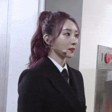 a woman with purple hair is wearing a suit and tie and has a microphone in her ear