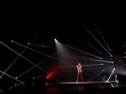 a woman in a long dress stands on a stage with a microphone