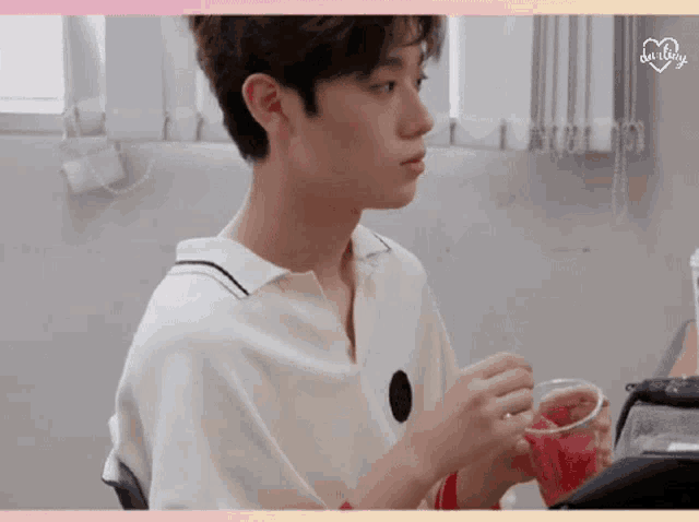 a boy in a white shirt is holding a glass of red liquid ..