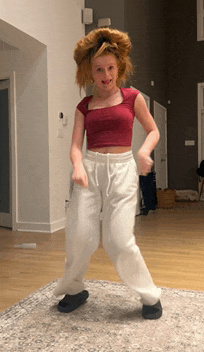 a girl in a red top and white sweatpants is dancing on the floor