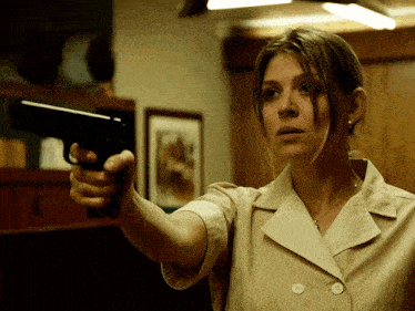 a woman in a tan jacket is pointing a gun
