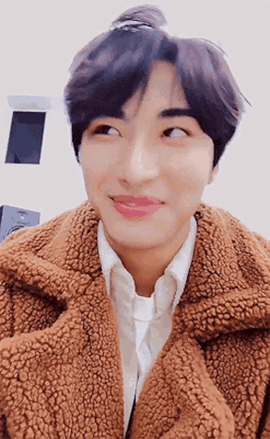 a young man wearing a brown jacket and a white shirt is making a face .