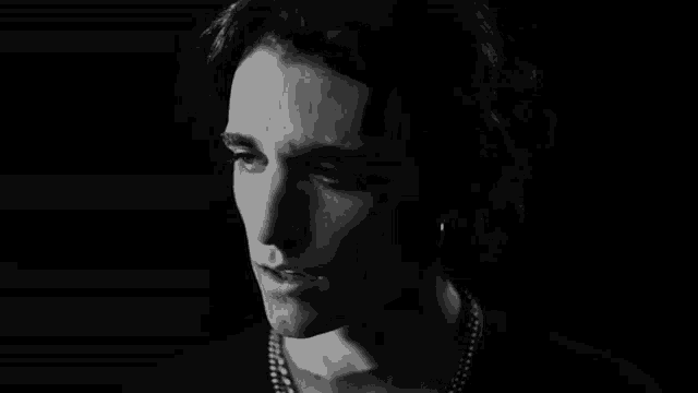 a black and white photo of a young man wearing a pearl necklace and earrings .