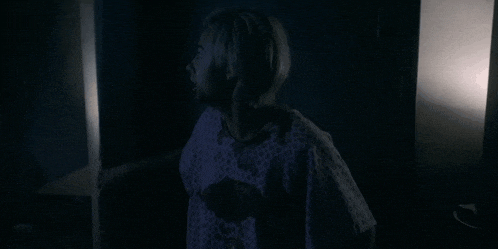 a woman in a hospital gown is standing in the dark in a dark room .