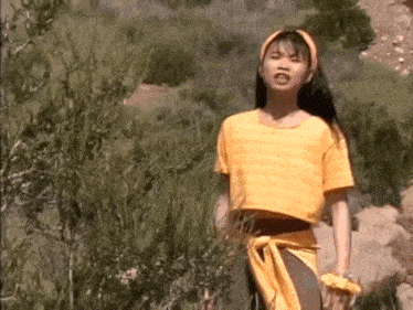a young girl wearing a yellow shirt and a yellow headband is standing in the grass .
