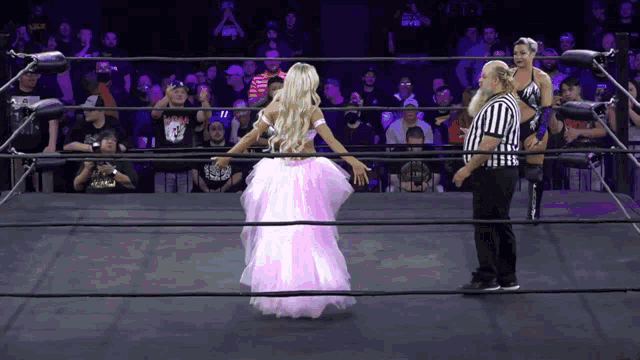 a woman in a pink dress is standing in a wrestling ring
