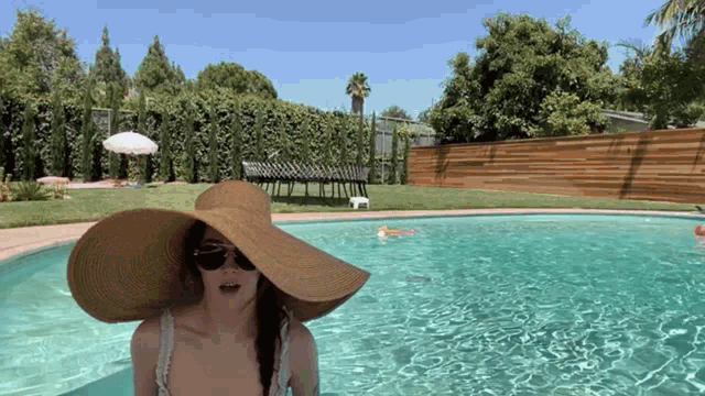 a woman wearing a straw hat and sunglasses is standing in a swimming pool