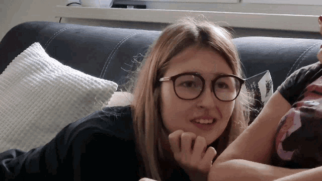 a young woman wearing glasses is laying on a couch