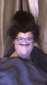 a woman with glasses and a messy bun is making a funny face .
