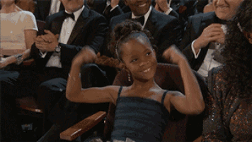 a little girl in a blue dress is sitting in a crowd of people applauding