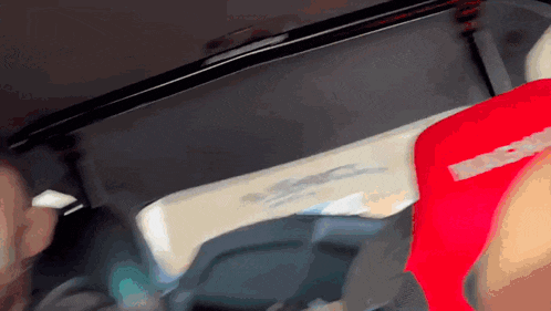 a person sitting in a car with a red shirt that says ' supreme ' on it