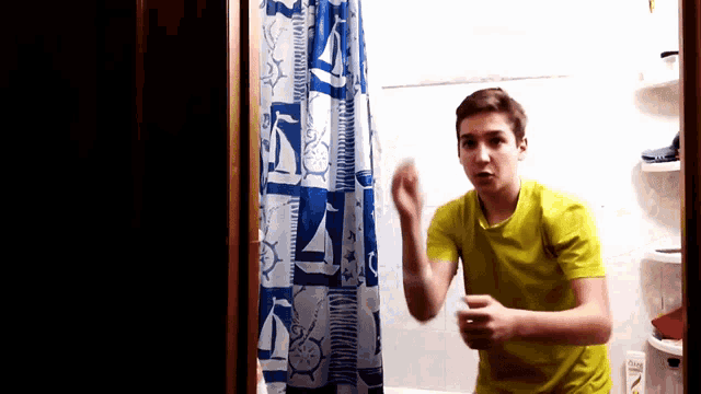 a young boy in a yellow shirt is standing in front of a shower curtain with sailboats on it